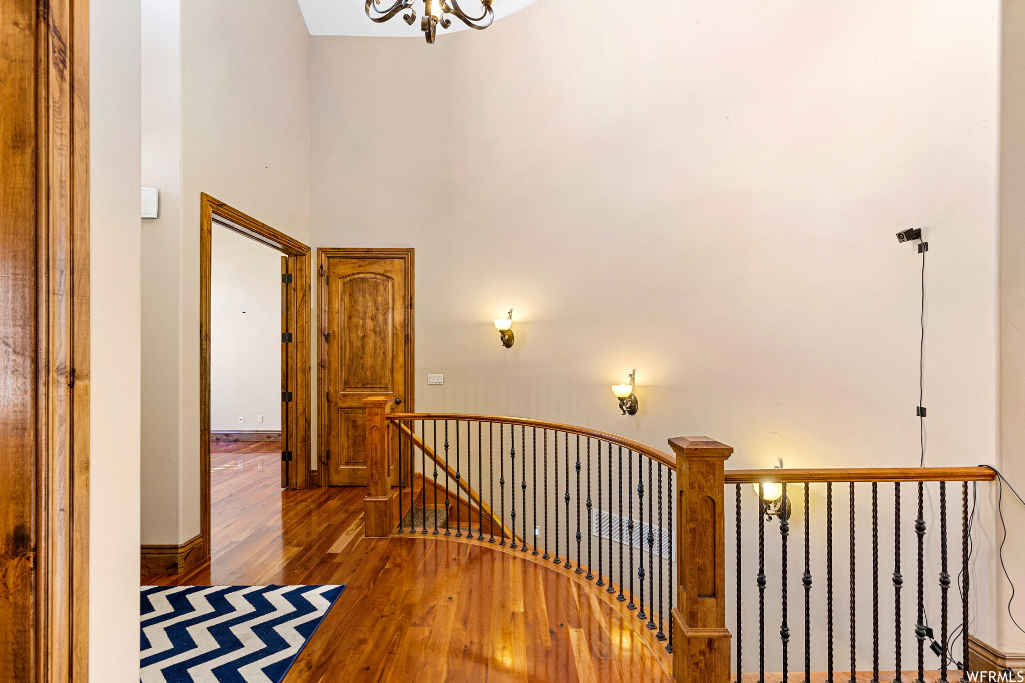 Hall featuring a towering ceiling, hardwood flooring, and a chandelier