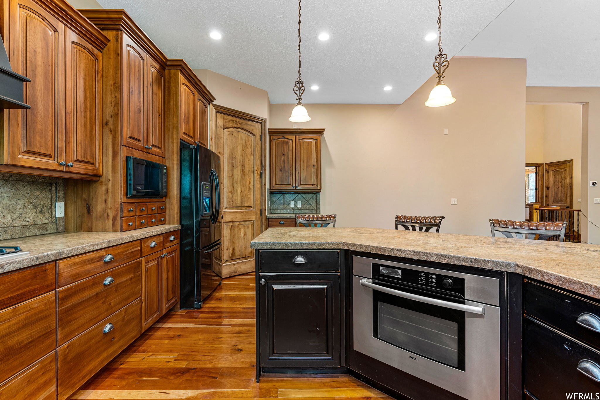 Kitchen featuring backsplash, decorative light fixtures, light hardwood floors, and black appliances