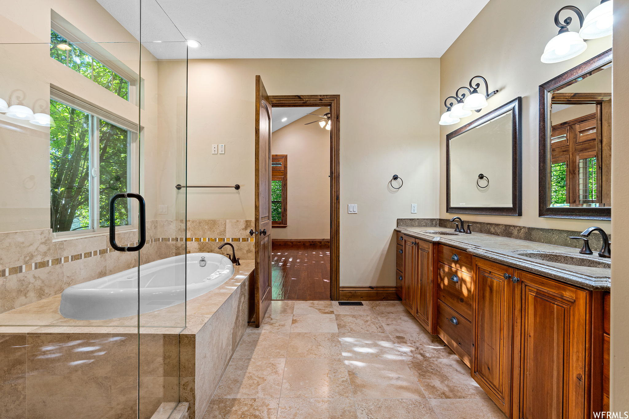 Bathroom featuring tiled tub, tile flooring, and dual bowl vanity