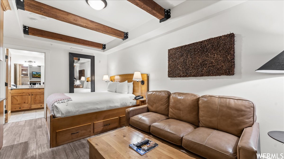 Tiled bedroom featuring ensuite bathroom and beamed ceiling