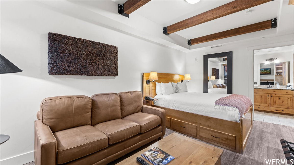 Tiled bedroom featuring connected bathroom and beamed ceiling