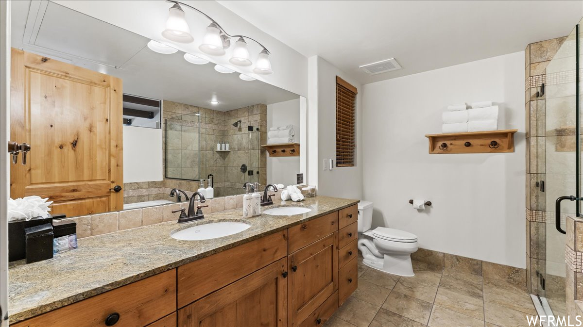 Bathroom with a shower with shower door, tile floors, toilet, and double sink vanity