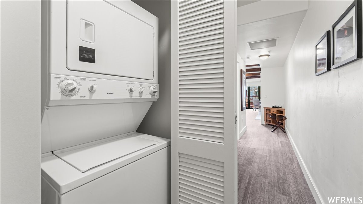 Laundry room featuring light carpet and stacked washing maching and dryer