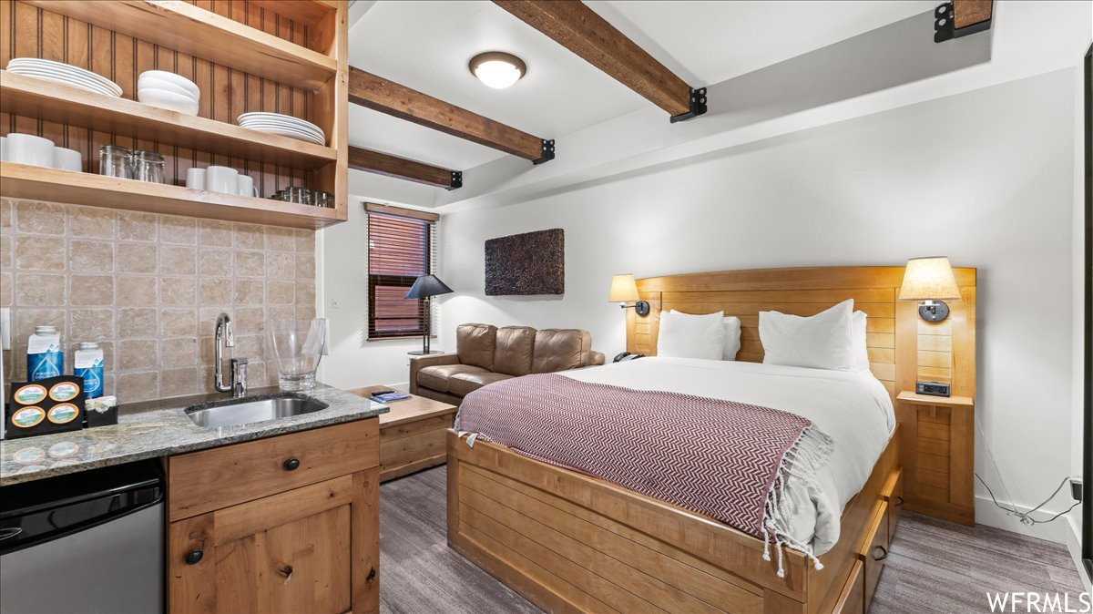 Hardwood floored bedroom featuring sink and beamed ceiling