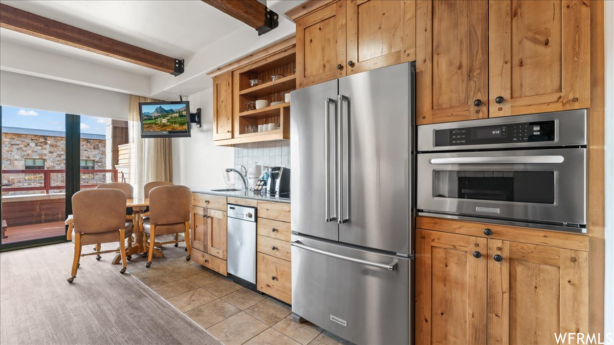 Kitchen featuring sink, light tile floors, backsplash, beamed ceiling, and appliances with stainless steel finishes