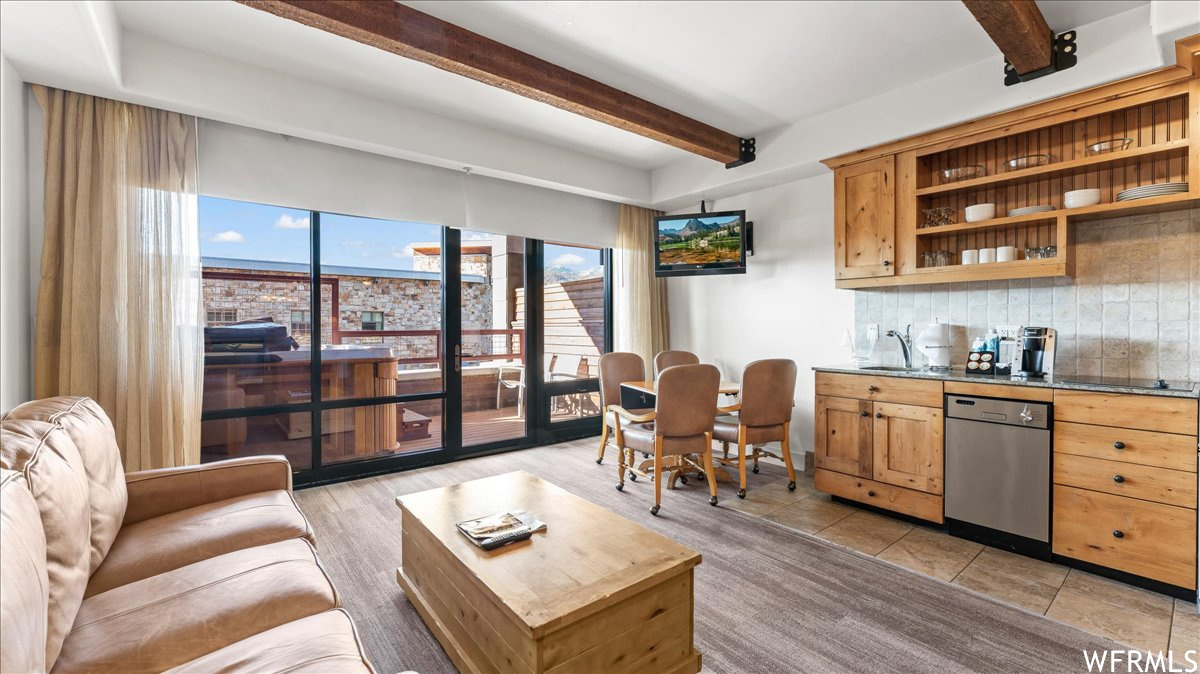 Interior space with light tile floors, stainless steel dishwasher, backsplash, sink, and beam ceiling