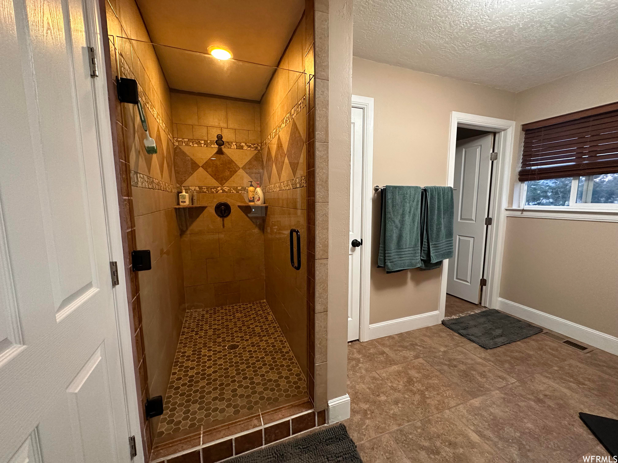 Bathroom featuring a textured ceiling, tile floors, and an enclosed shower