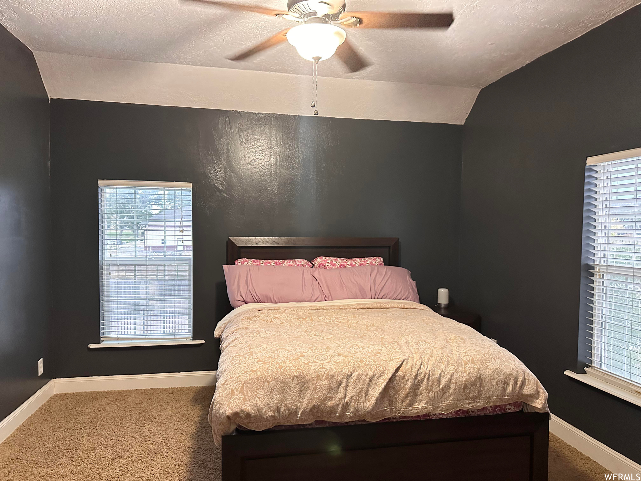 Bedroom with vaulted ceiling, ceiling fan, dark colored carpet, and a textured ceiling