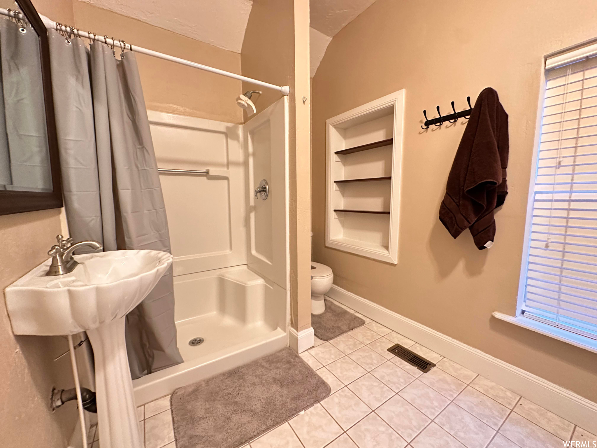 Bathroom featuring sink, toilet, vaulted ceiling, curtained shower, and tile floors