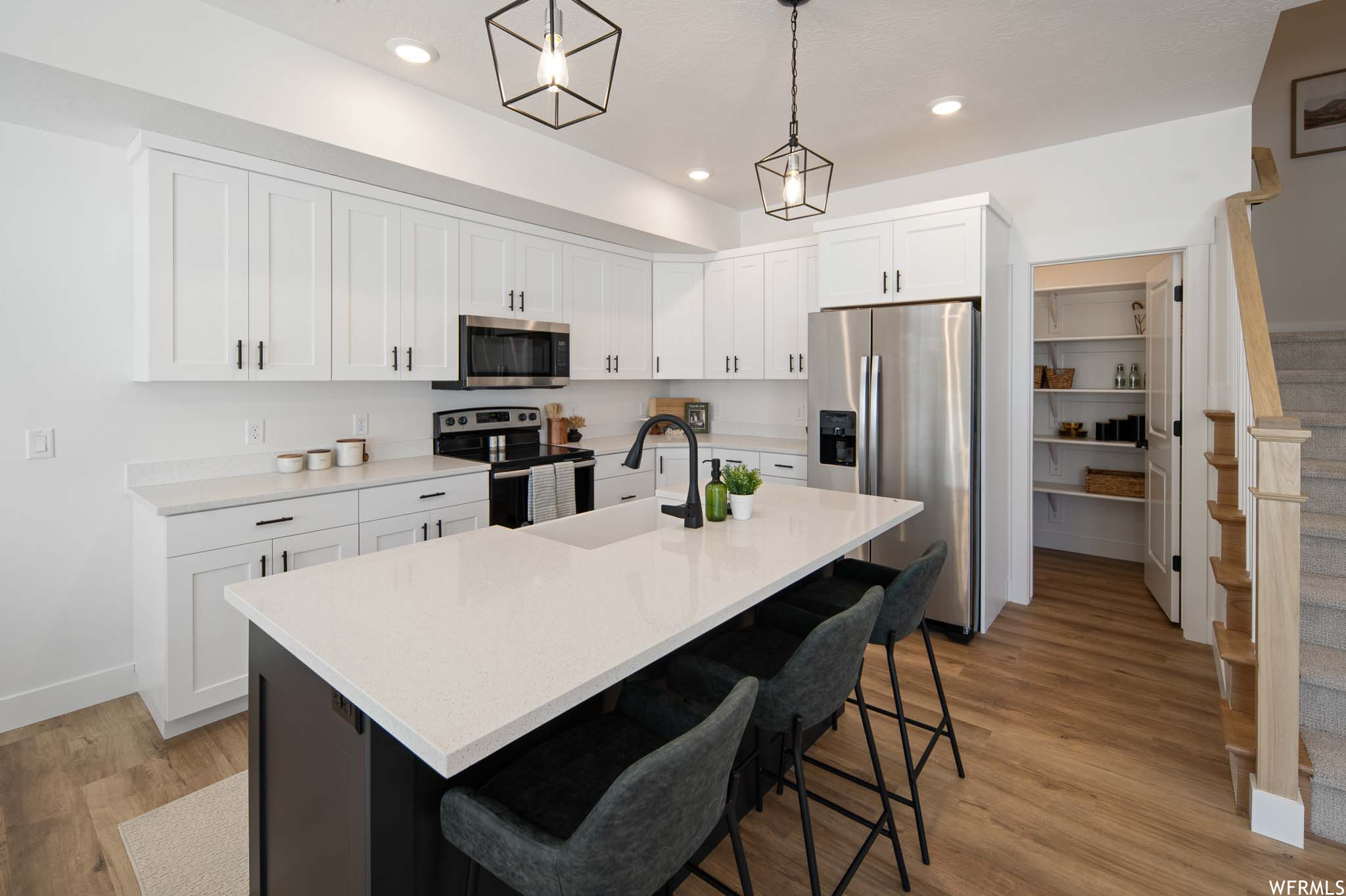 Kitchen featuring pendant lighting, white cabinetry, light hardwood floors, and appliances with stainless steel finishes