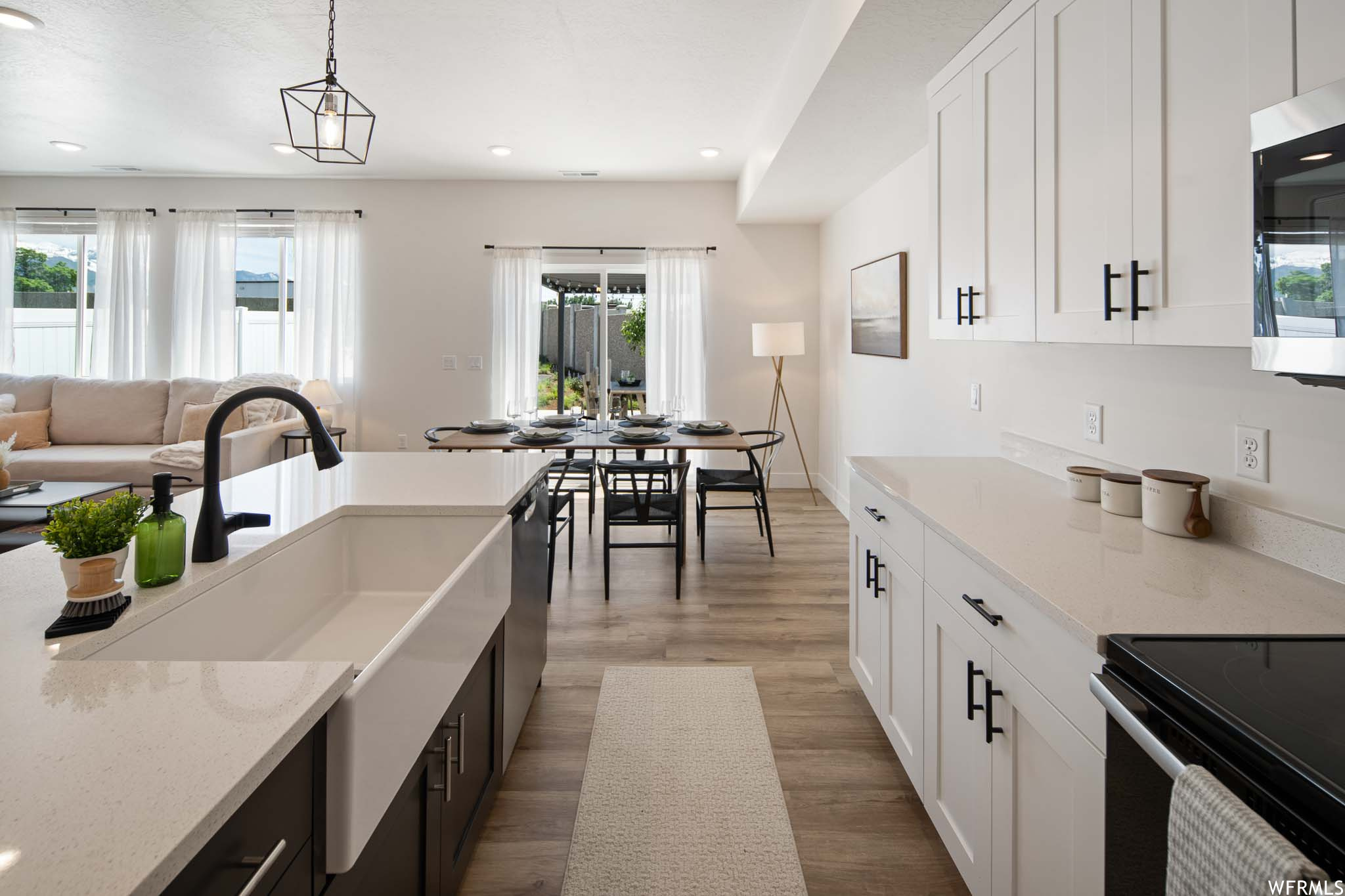 Kitchen featuring a wealth of natural light, white cabinets, light hardwood floors, and hanging light fixtures