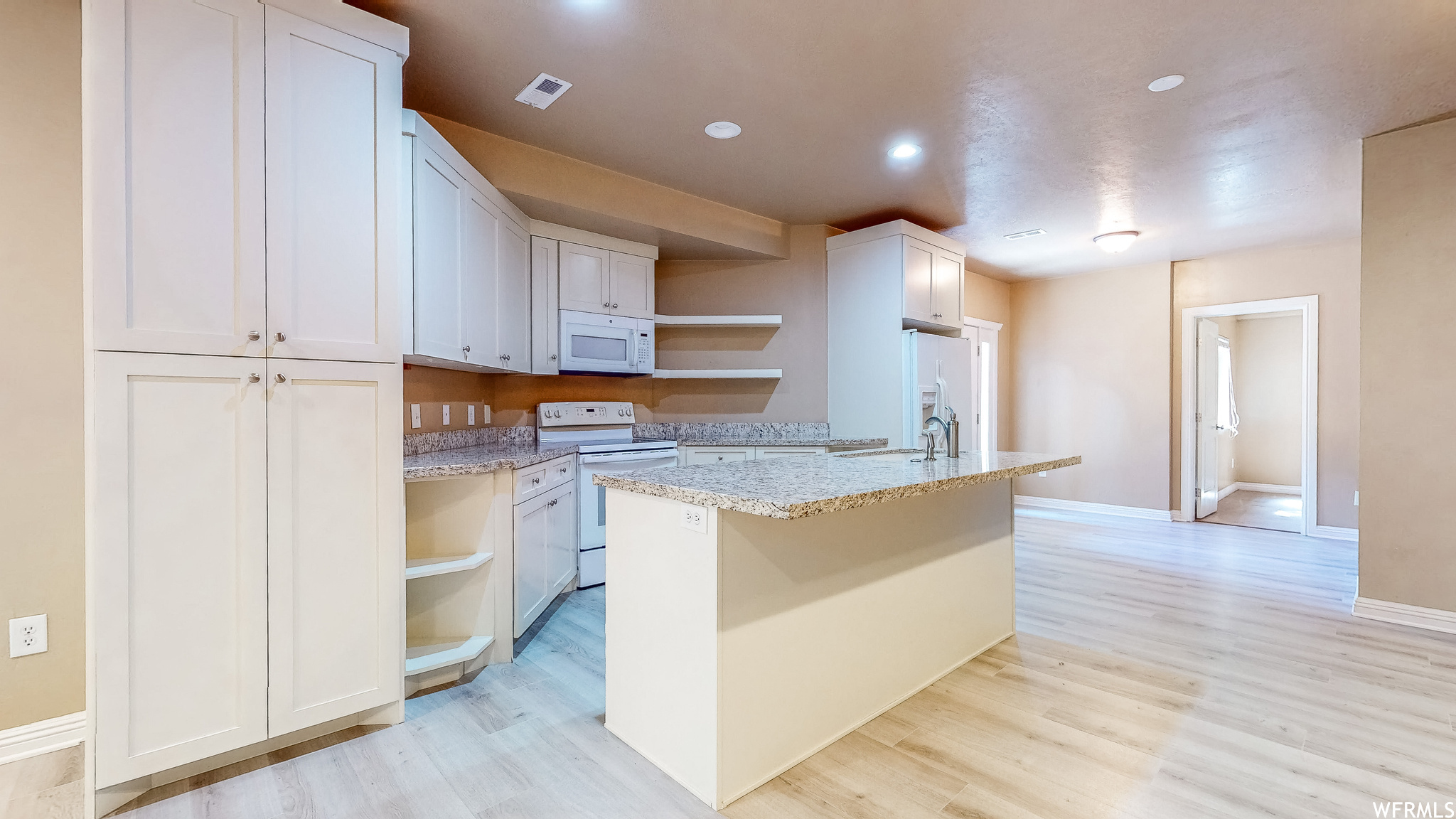 Full basement kitchen with light hardwood / wood-style flooring, light stone countertops, an island with sink.