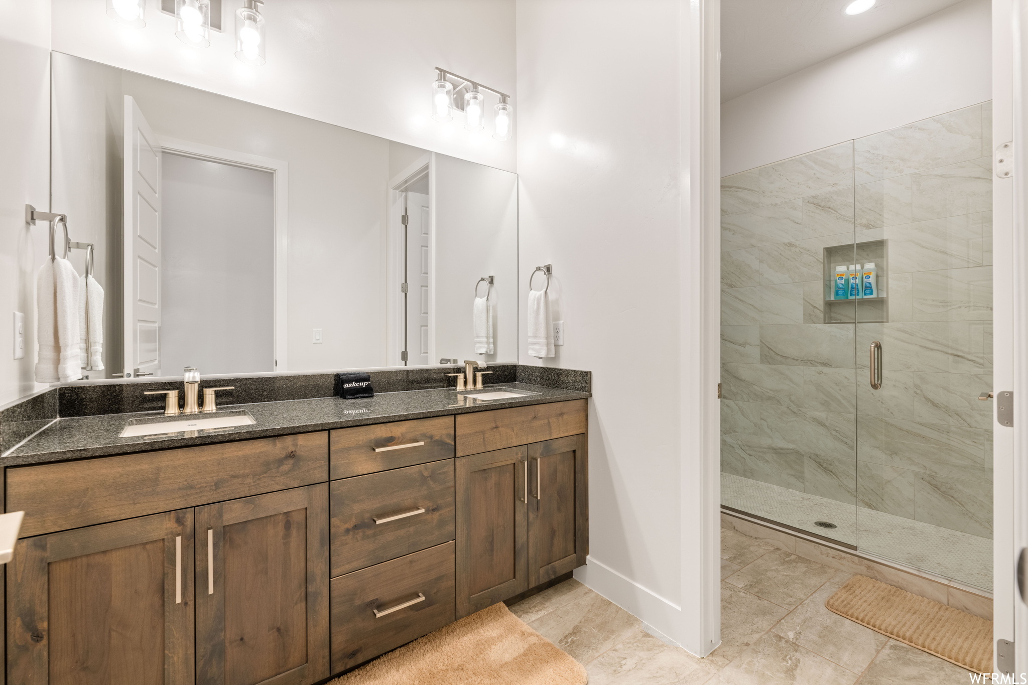 Bathroom featuring an enclosed shower, double sink vanity, and tile floors