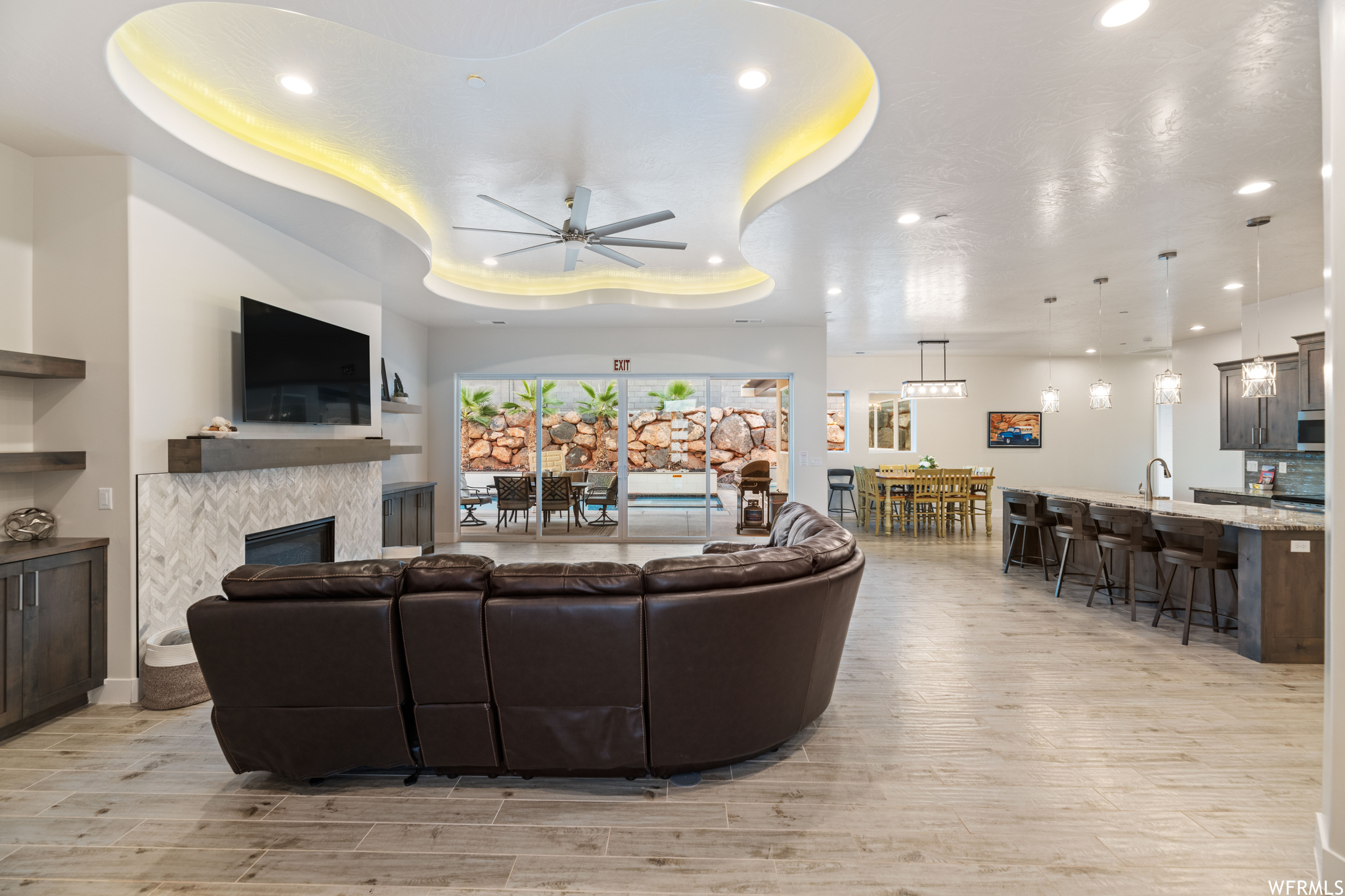 Living room featuring a tray ceiling, light hardwood / wood-style floors, sink, ceiling fan, and a tiled fireplace