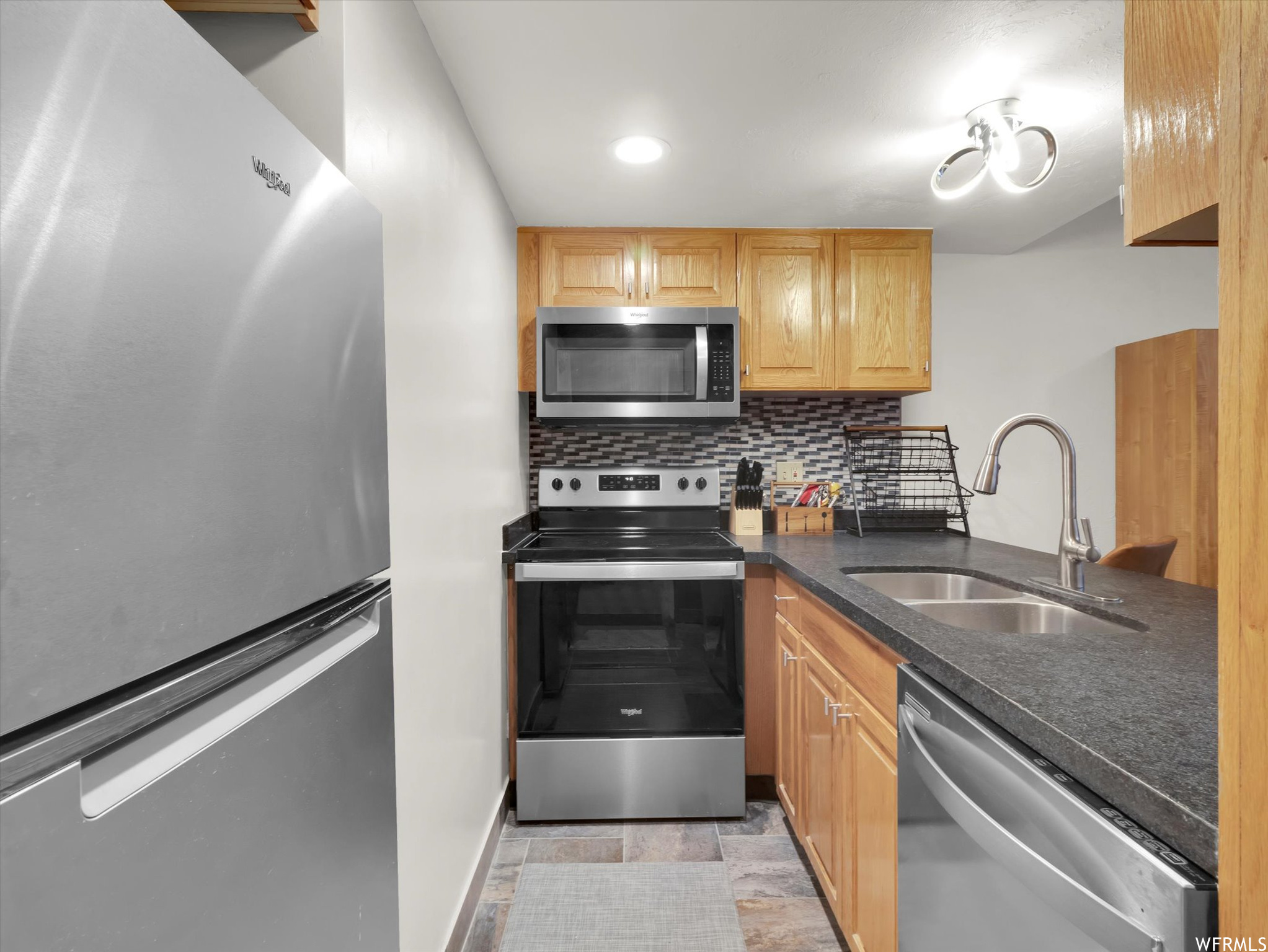 Kitchen with light tile floors, tasteful backsplash, sink, and appliances with stainless steel finishes