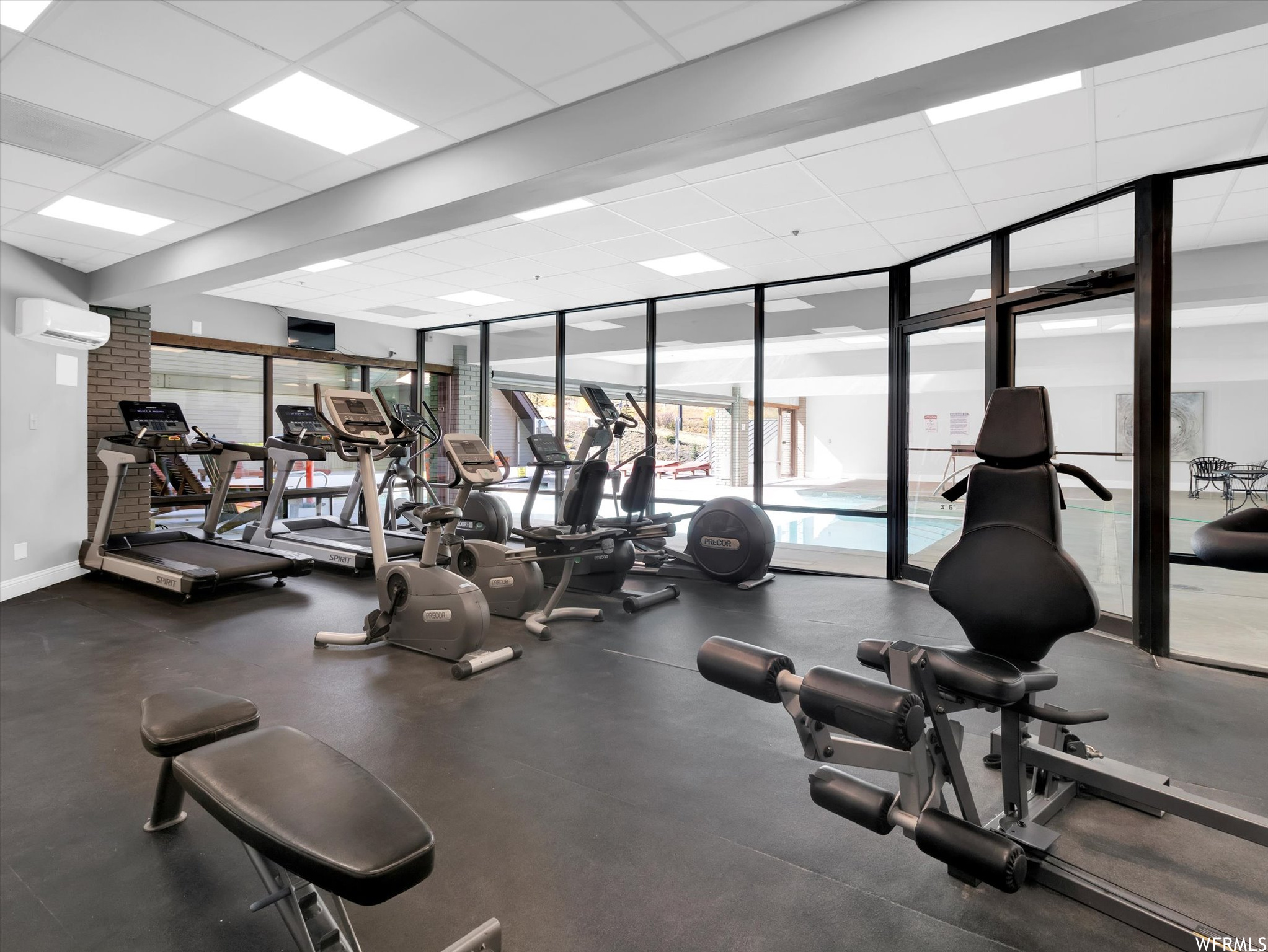 Gym with expansive windows, a wall mounted air conditioner, and a paneled ceiling