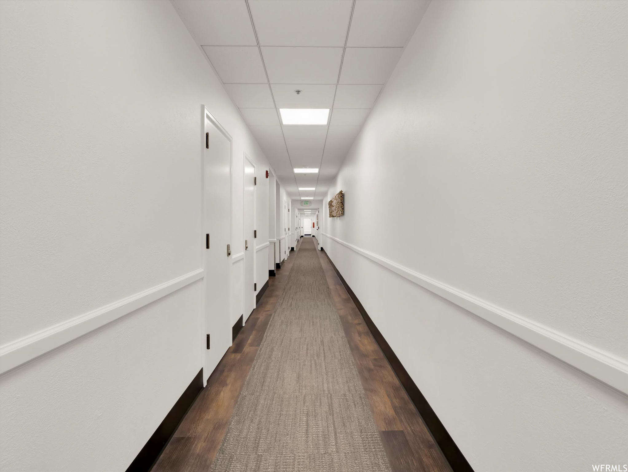 Corridor with a drop ceiling and dark hardwood floors