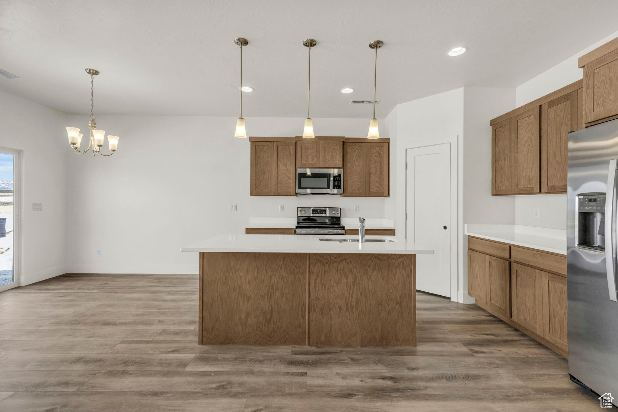 Kitchen with light wood-type flooring, stainless steel appliances, a chandelier, hanging light fixtures, and a kitchen island with sink