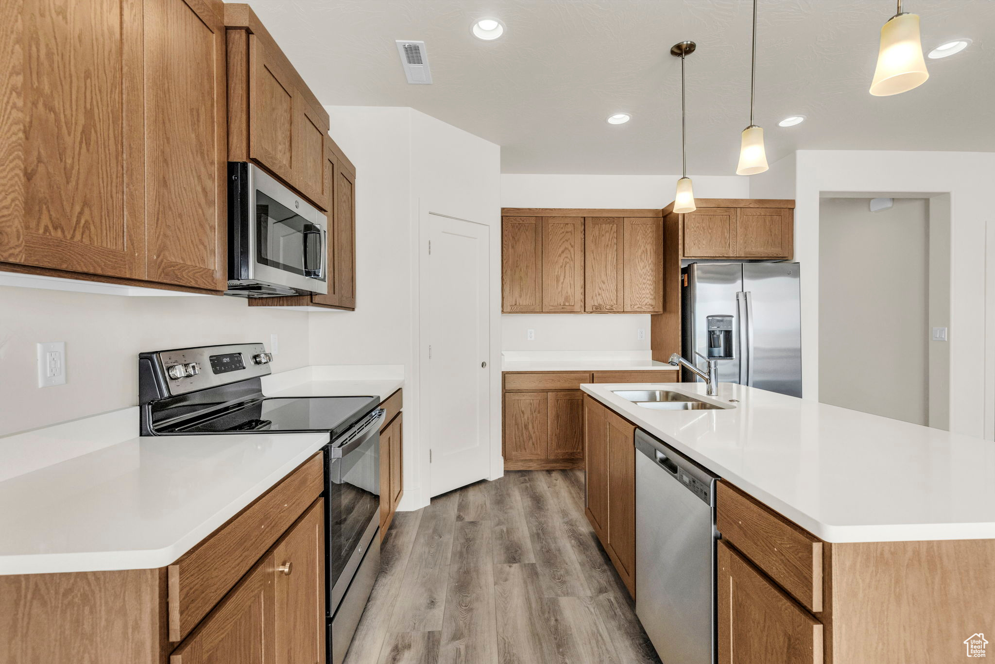 Kitchen with appliances with stainless steel finishes, light hardwood / wood-style floors, an island with sink, sink, and decorative light fixtures