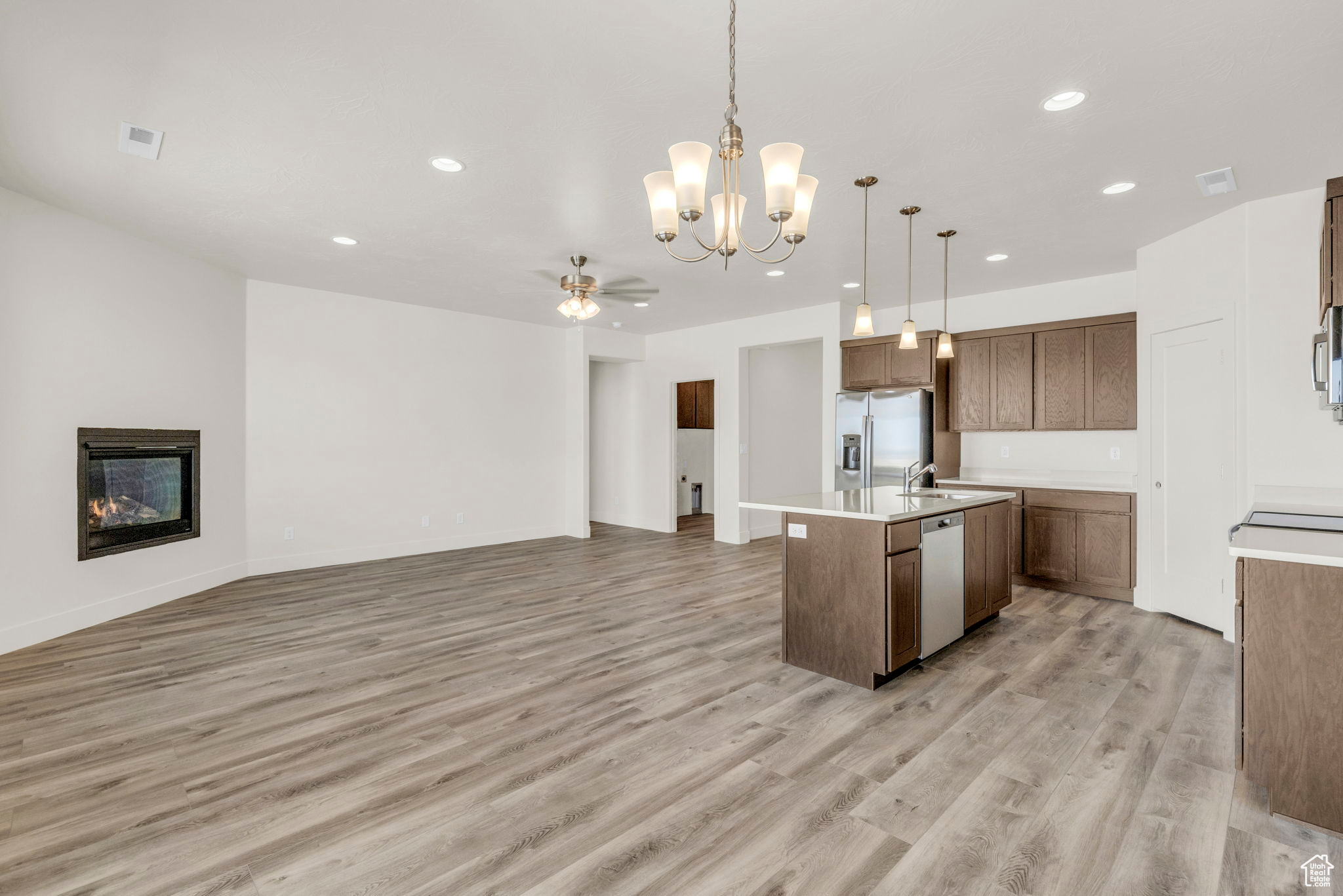Kitchen featuring ceiling fan with notable chandelier, stainless steel appliances, light hardwood / wood-style flooring, an island with sink, and decorative light fixtures