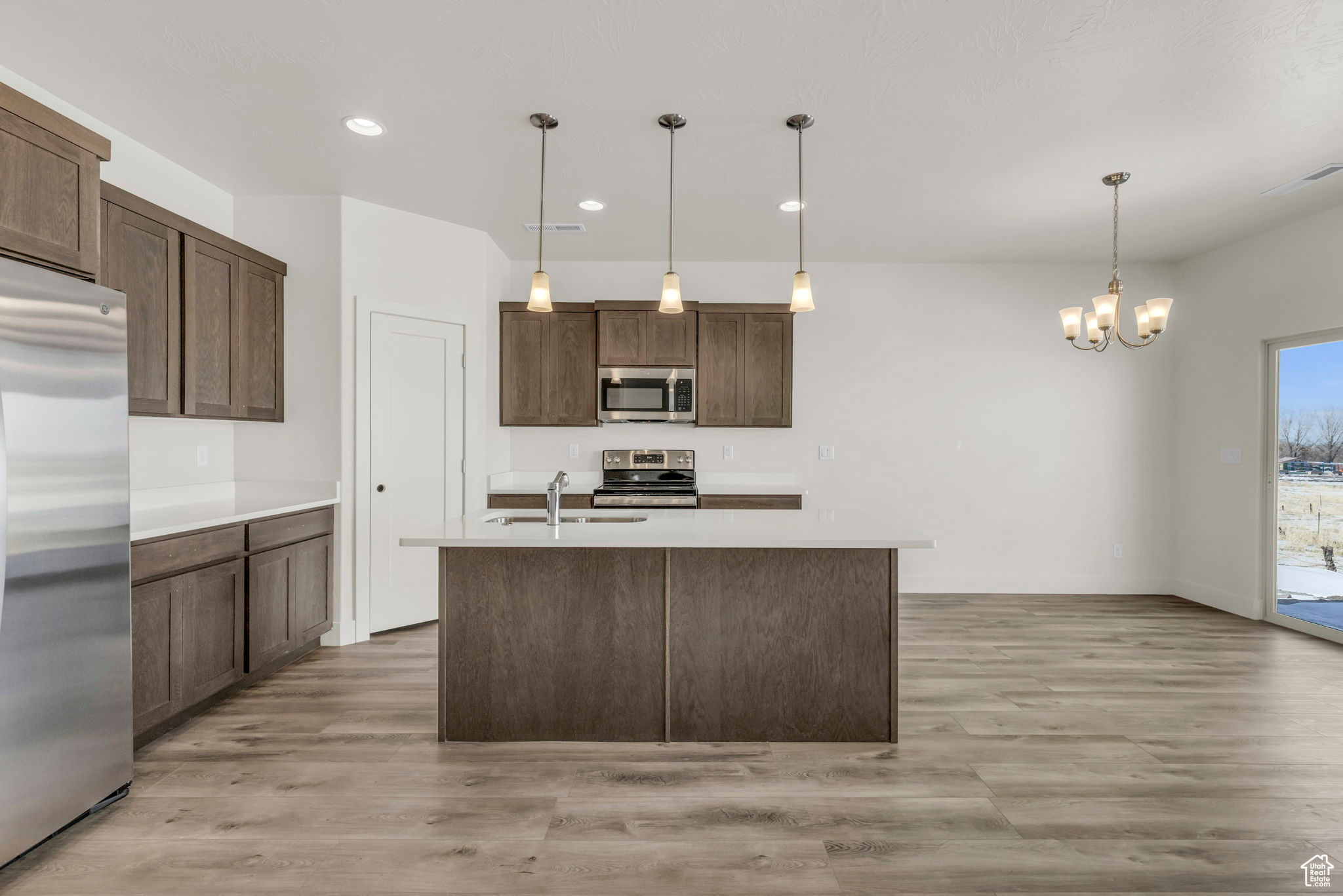 Kitchen featuring light wood-type flooring, dark brown cabinets, stainless steel appliances, pendant lighting, and a chandelier