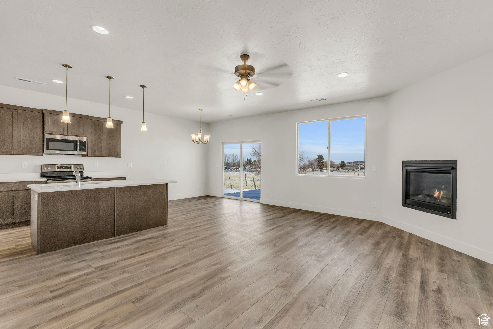 Kitchen featuring pendant lighting, appliances with stainless steel finishes, light hardwood / wood-style floors, and ceiling fan with notable chandelier