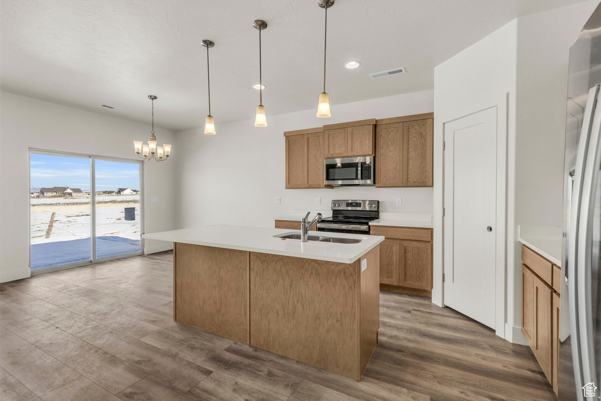 Kitchen with light hardwood / wood-style flooring, appliances with stainless steel finishes, decorative light fixtures, and a center island with sink