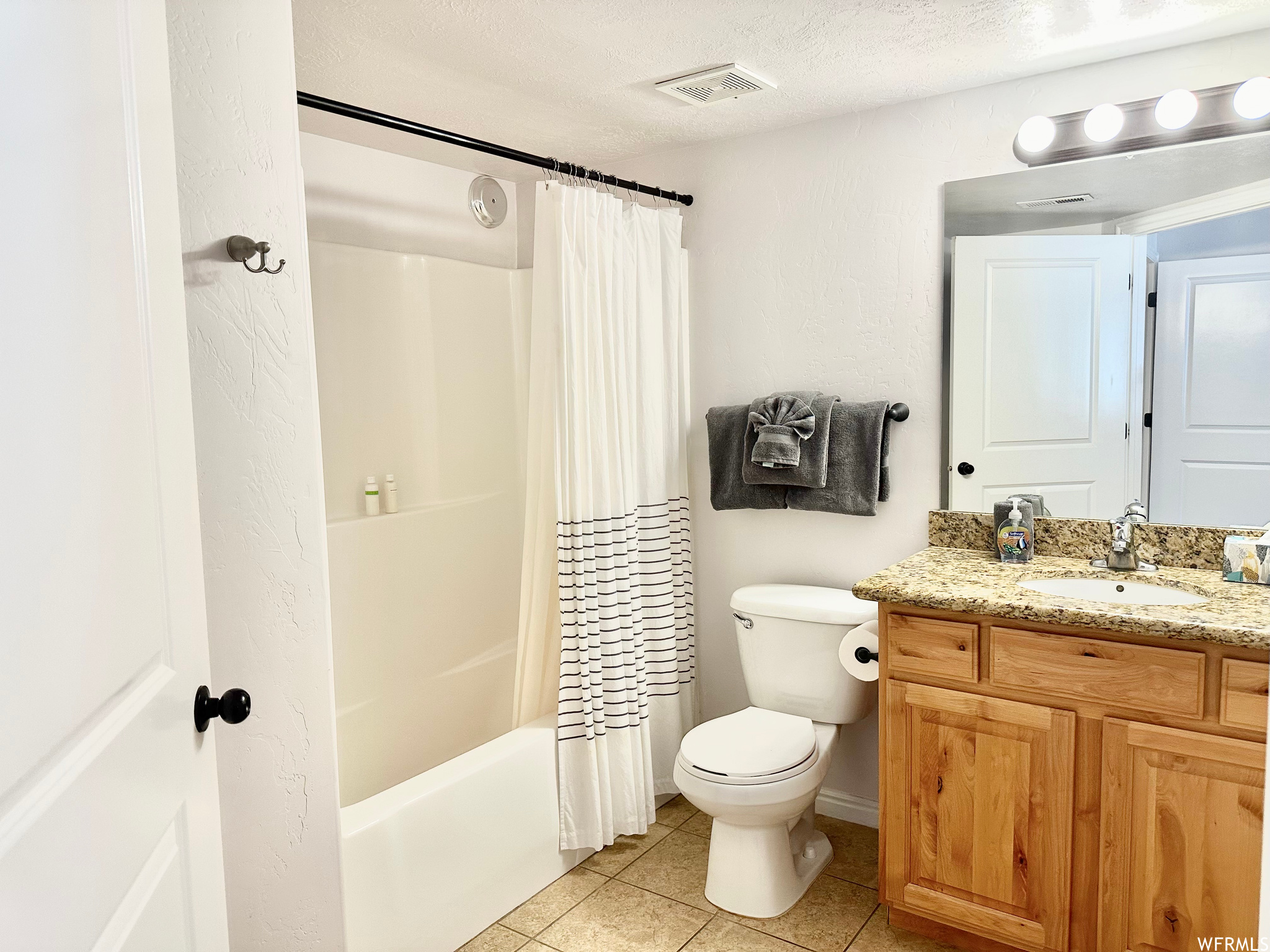 Full bathroom featuring large vanity, toilet, tile floors, a textured ceiling, and shower / bath combo with shower curtain