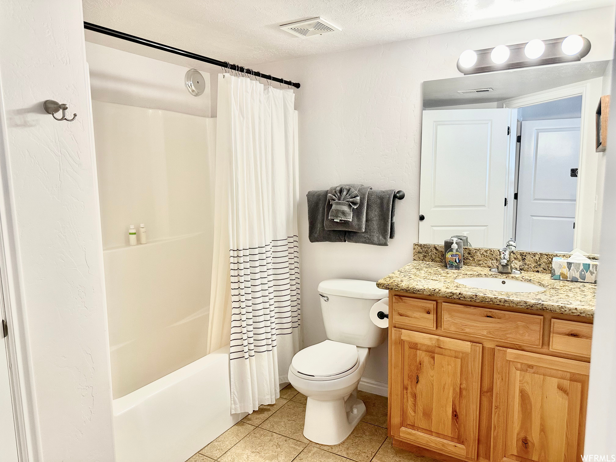 Full bathroom with toilet, a textured ceiling, large vanity, tile floors, and shower / tub combo with curtain