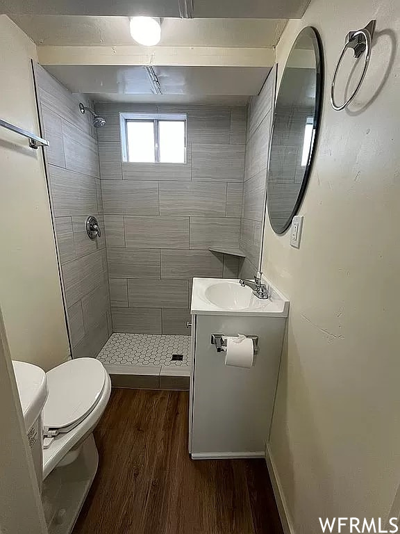 Bathroom featuring a tile shower, vanity, hardwood floors, and toilet