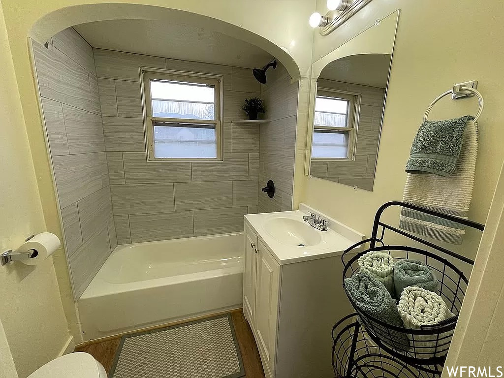 Bathroom with wood-type flooring, large vanity, tiled shower / bath, and a wealth of natural light