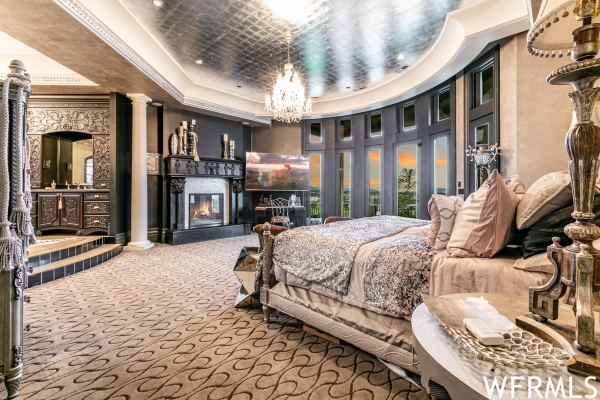 Bedroom with a fireplace, decorative columns, crown molding, an inviting chandelier, and a tray ceiling