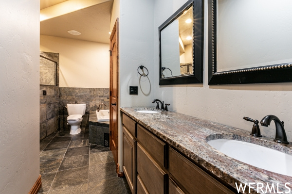 Bathroom featuring toilet, tile walls, tile floors, a bathing tub, and double sink vanity