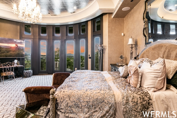 Carpeted bedroom with a towering ceiling, access to exterior, a raised ceiling, and a notable chandelier