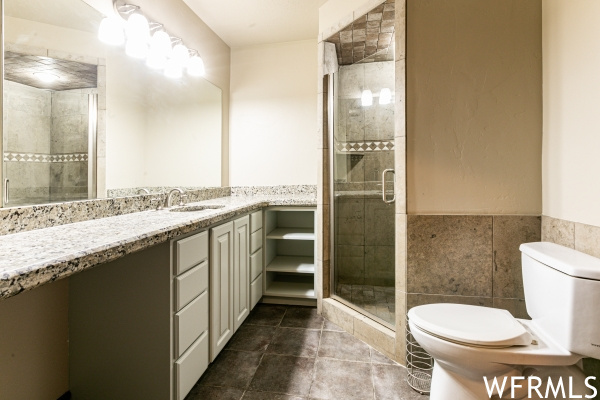 Bathroom featuring toilet, vanity, a shower with shower door, tile walls, and tile floors