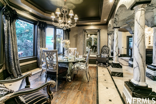 Dining area with a tray ceiling, an inviting chandelier, decorative columns, and crown molding