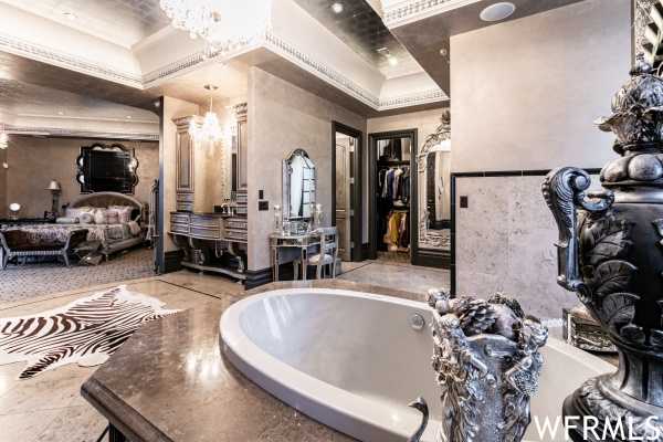 Bathroom with a bath to relax in, a notable chandelier, vanity, crown molding, and a tray ceiling