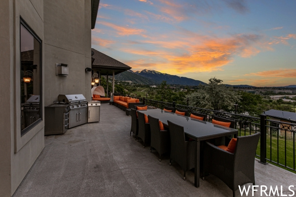 Patio terrace at dusk featuring a balcony, grilling area, and a mountain view
