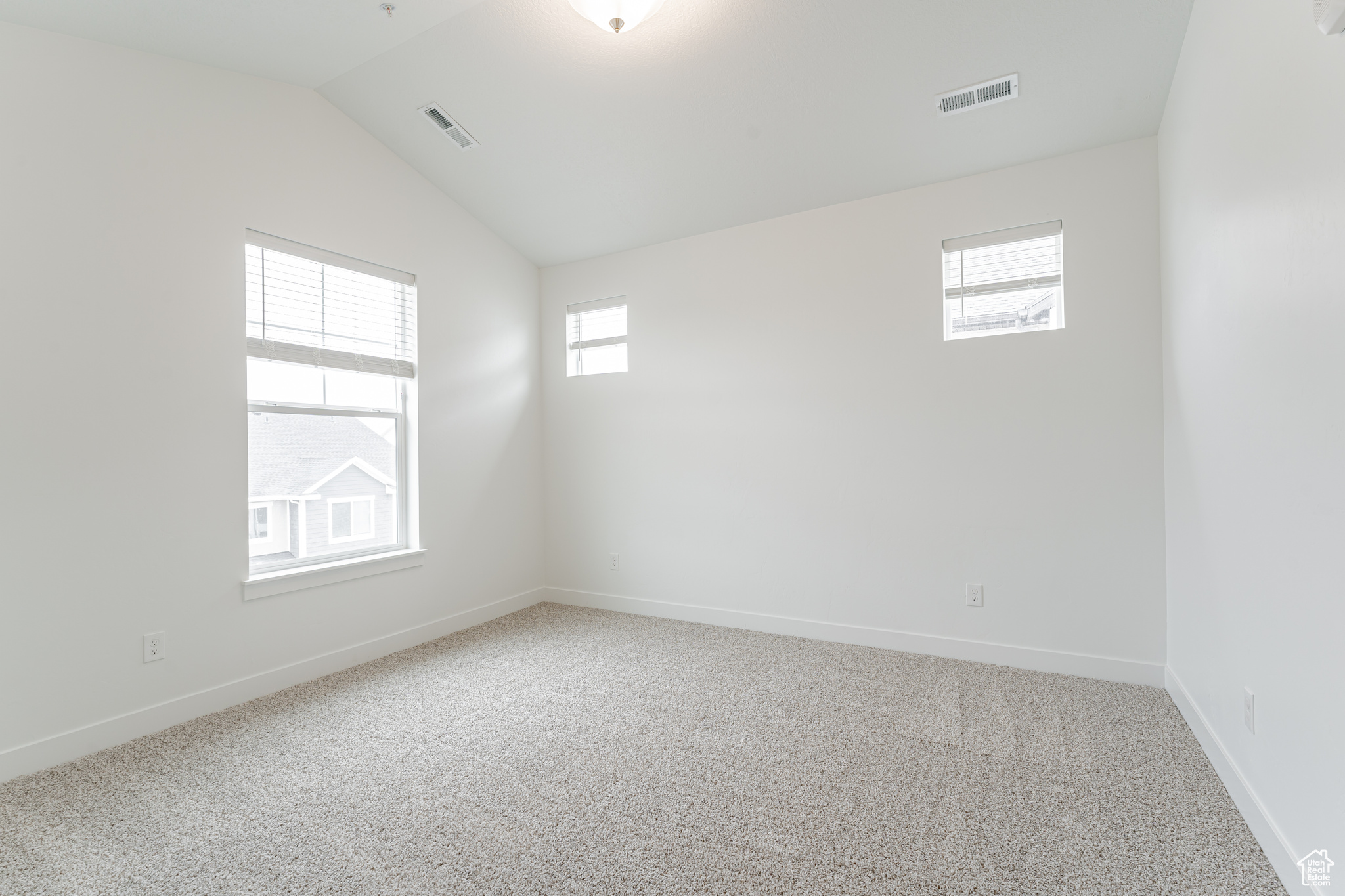 Unfurnished room featuring light colored carpet and vaulted ceiling