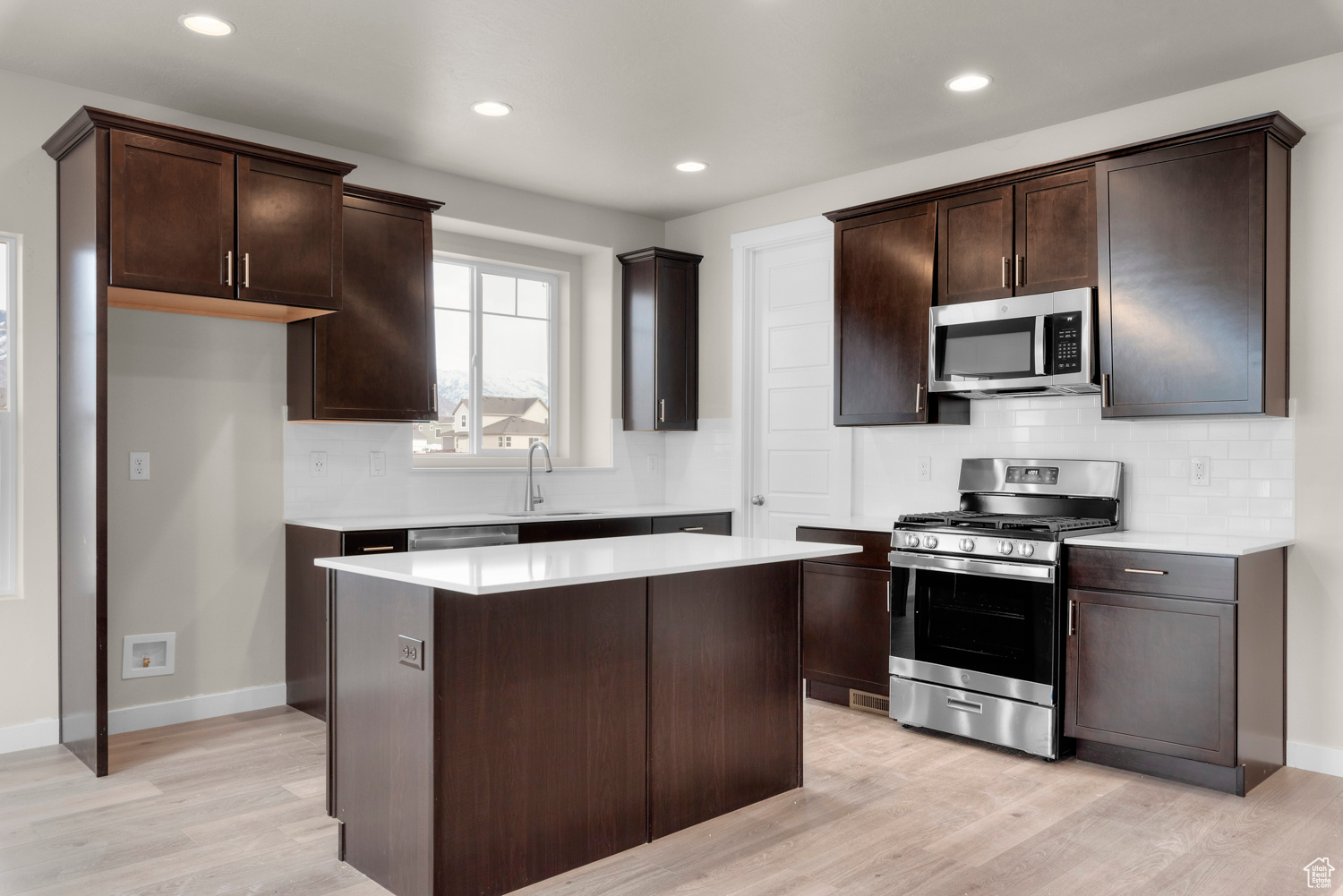 Kitchen with tasteful backsplash, stainless steel appliances, light wood-type flooring, and a kitchen island