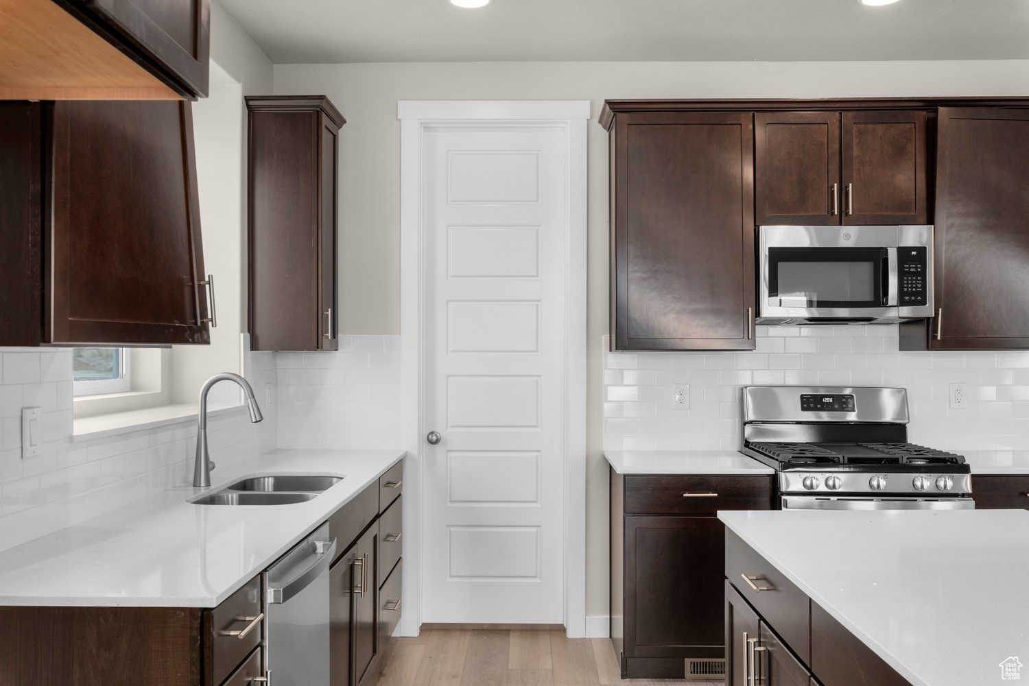 Kitchen with light hardwood / wood-style floors, stainless steel appliances, dark brown cabinets, tasteful backsplash, and sink