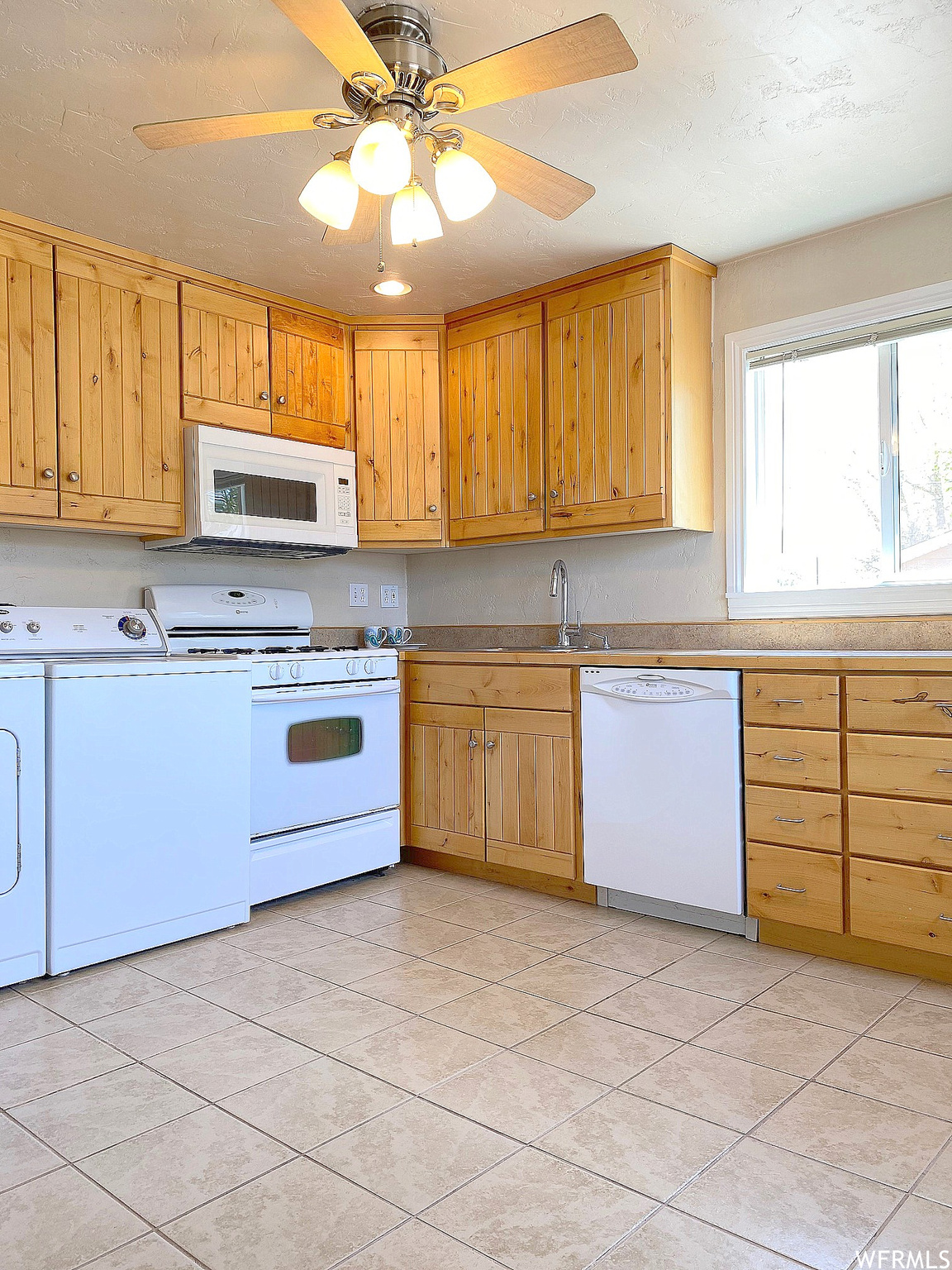 Kitchen featuring white appliances, washing machine and dryer, light tile floors, and ceiling fan