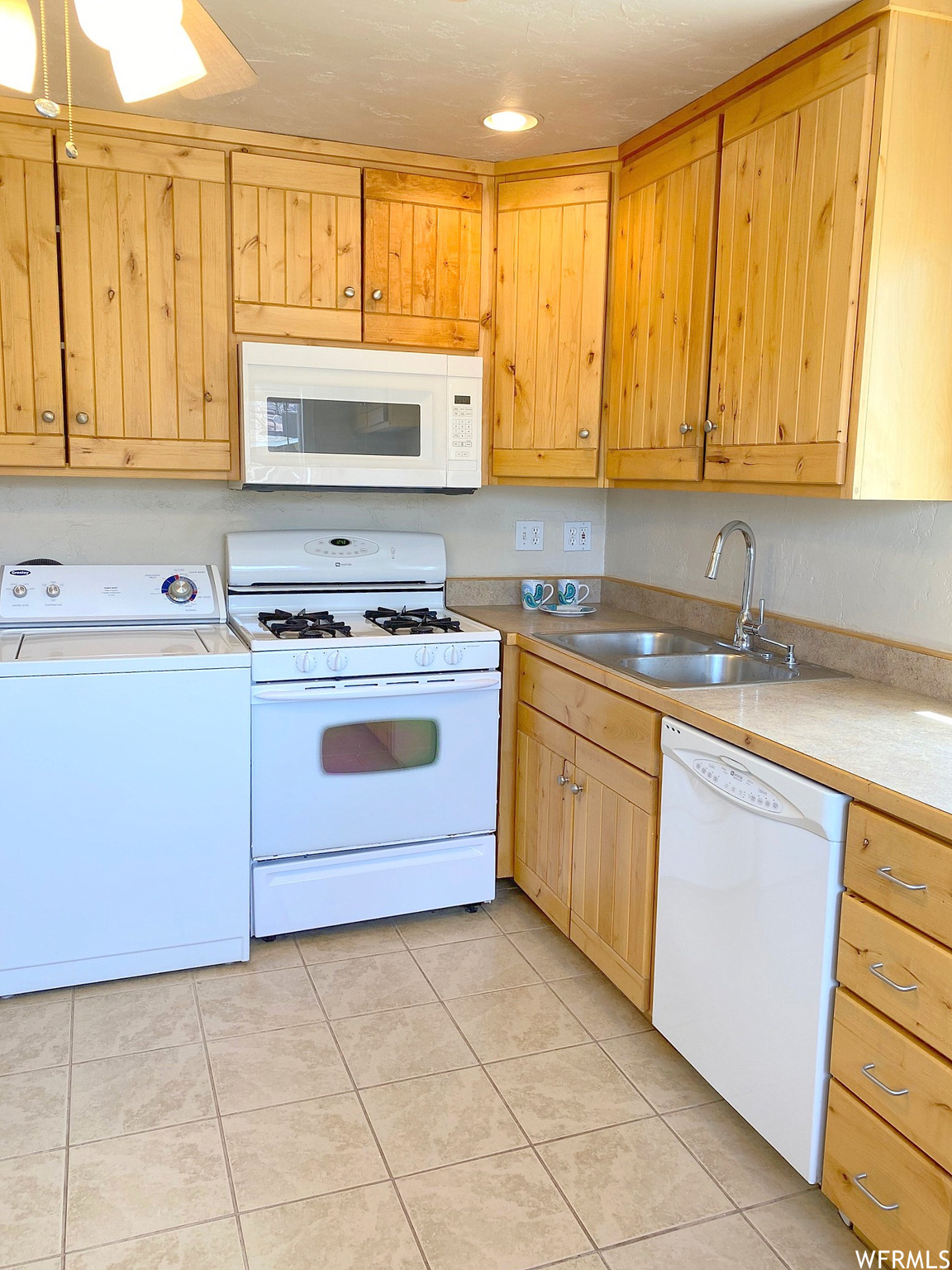 Kitchen featuring white appliances, sink, light tile floors, and washer / clothes dryer