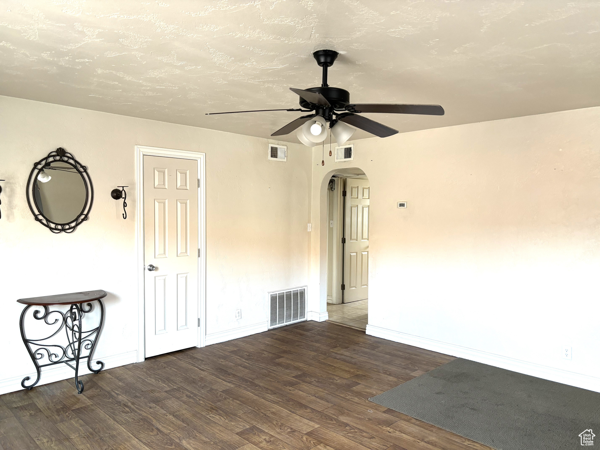 Empty room coat closet and arched entry to the rest of the home. with dark hardwood / wood-style floors and ceiling fan