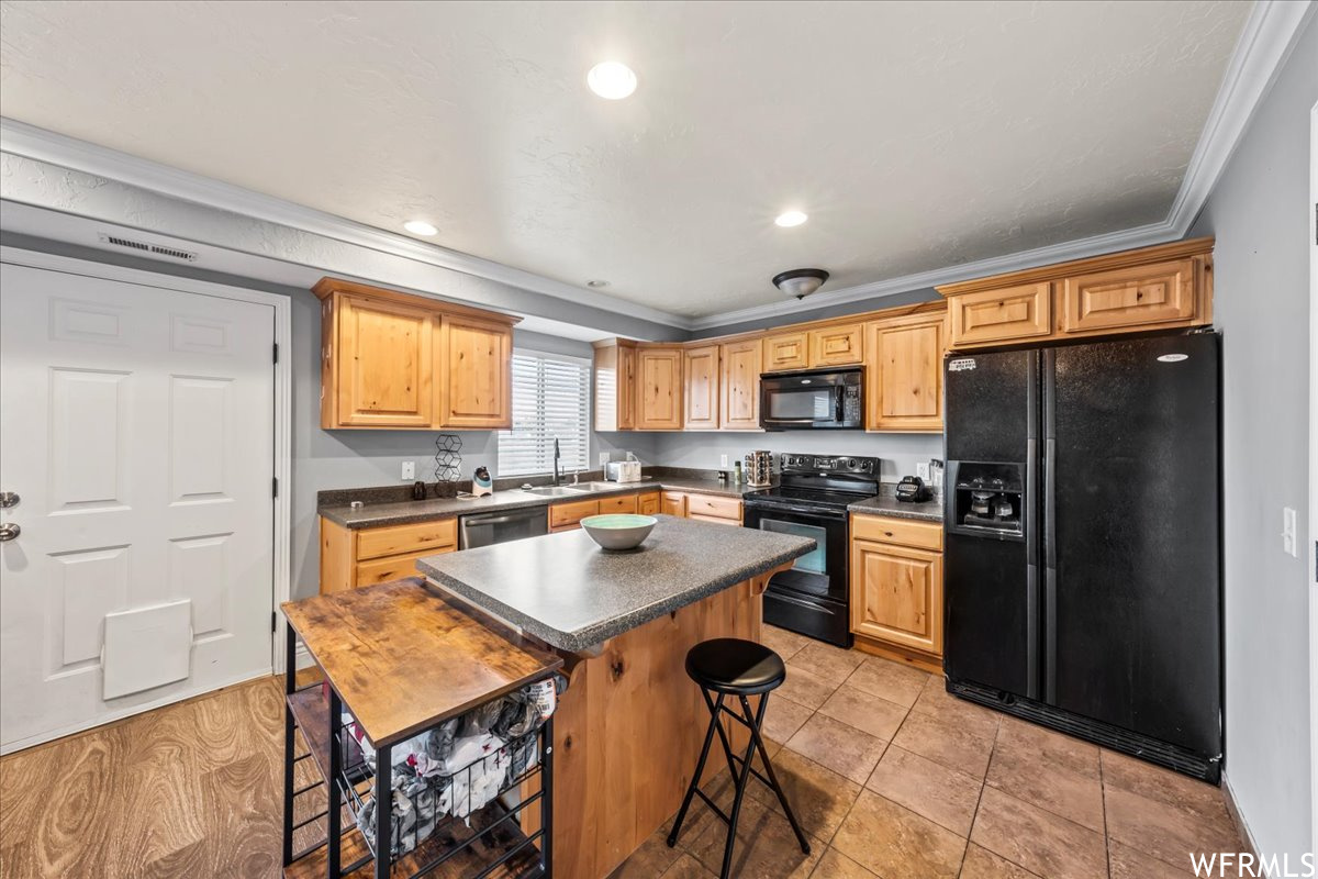 Kitchen with a center island, sink, black appliances, a breakfast bar, and ornamental molding