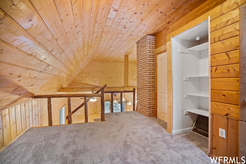 Additional living space featuring light carpet, wooden walls, brick wall, vaulted ceiling, and wooden ceiling