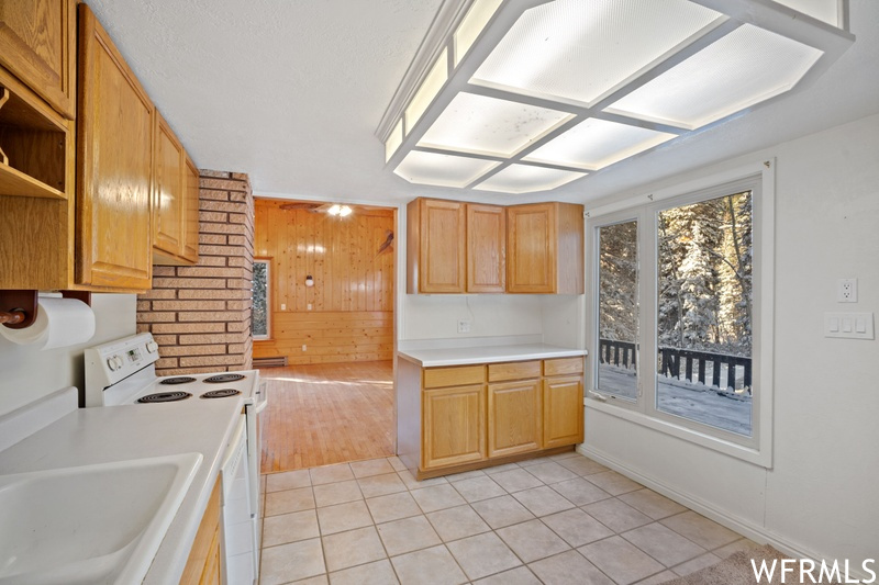 Kitchen with wood walls, white electric range, light tile floors, and sink