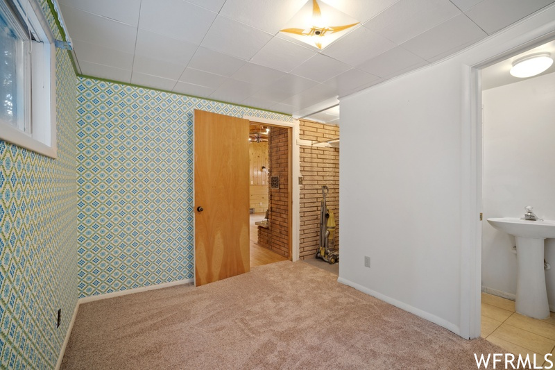 Unfurnished bedroom with sink, light carpet, brick wall, ensuite bathroom, and a fireplace