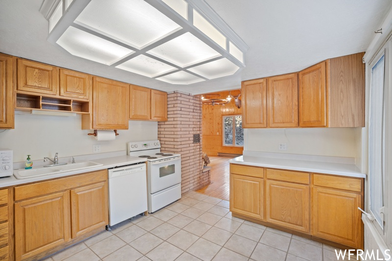 Kitchen with white appliances, sink, light tile floors, and brick wall