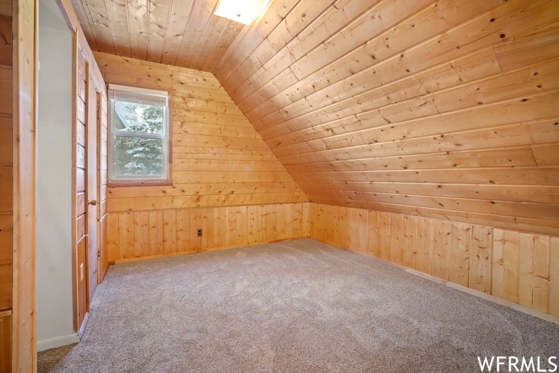 Bonus room featuring light carpet, lofted ceiling, wood walls, and wooden ceiling